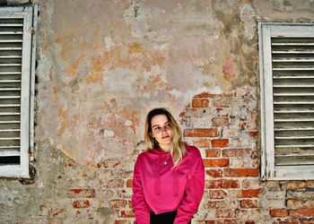 Portrait of a smiling young woman standing against brick wall