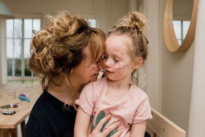 Mother and daughter hugging whilst playing with make up at home