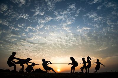 Silhouette people playing against sky during sunset