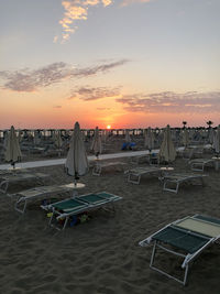 Chairs on beach against sky during sunset