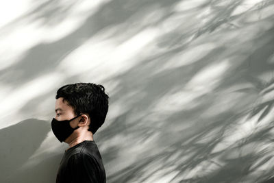 Side view of boy wearing mask standing against wall outdoors