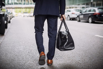 Low section of male lawyer carrying bag while walking on street