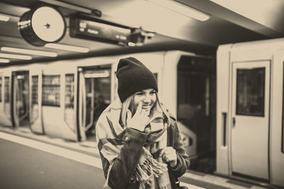 Smiling young woman walking on subway platform against train