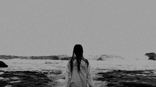 Rear view of woman standing at beach against clear sky