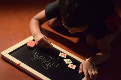 High angle view of girl writing on slate while sitting on floor at home