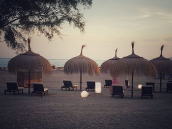 Chairs on beach against sky at sunset