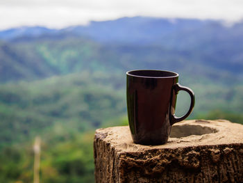 Close-up of coffee cup on wood against mountain