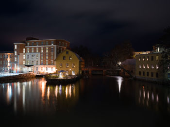 Illuminated buildings by river against sky at night