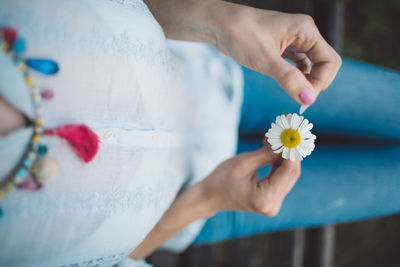 Midsection of woman with daisy sitting on bench