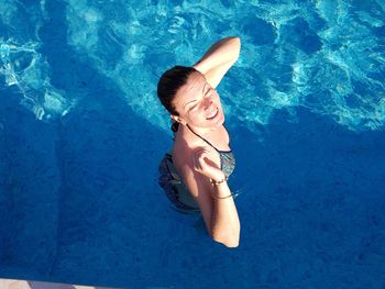 High angle view of smiling woman standing in swimming pool during sunny day
