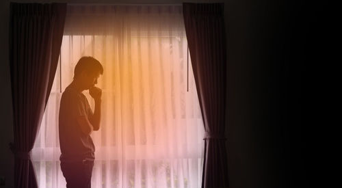 Silhouette woman standing by window at home