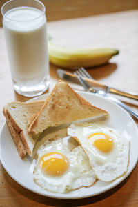 Close-up of fried eggs and breads in plate by milk glass on table