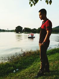 Side view of young woman standing on river against sky