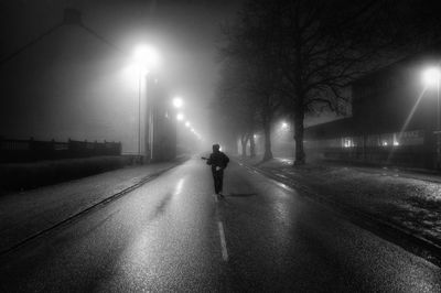 Rear view of guitarist walking on illuminated road at night