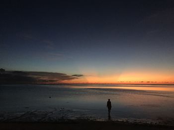 Silhouette man standing on beach against sky during sunset