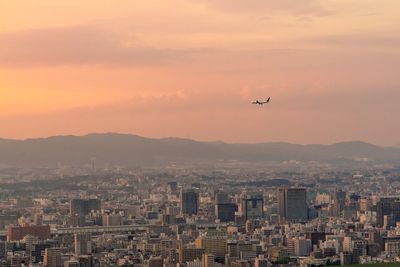 View of airplane flying over city against sky during sunset