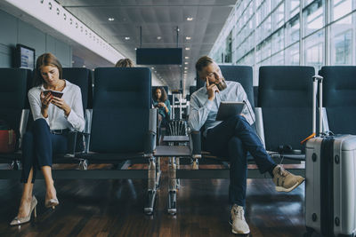 Thoughtful businessman looking away while sitting by female colleague at waiting area in airport