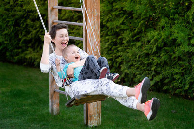 Cheerful woman with son swinging at park