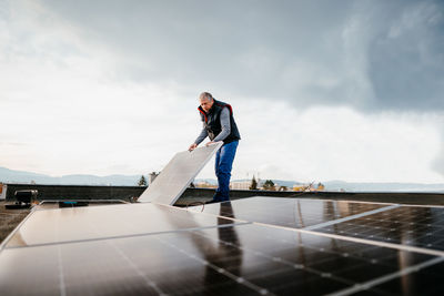 Man picking up solar panel while standing on roof