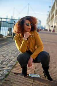 Woman wearing sunglasses crouching on street