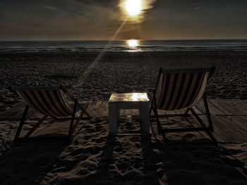 Chairs and table on beach against sky during sunset