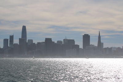 Sea by modern buildings against sky during sunset