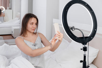 Female blogger recording vlog video on smartphone at home online influencer on near bed. streaming