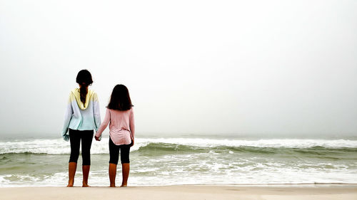 Rear view of girls standing at beach against clear sky