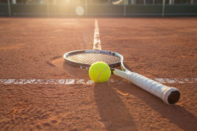 Close-up of tennis racket and ball on court during sunset