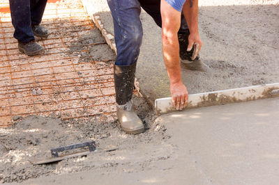Low section of manual worker scrapping on cement at construction site