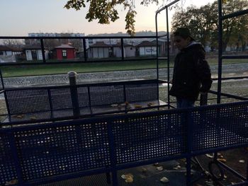 Side view of man sitting on railing against sky