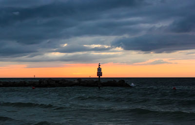 Lighthouse by sea against sky during sunset