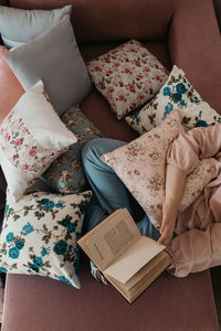 High angle view of woman reading book sitting on sofa at home