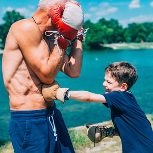 Shirtless grandfather with grandson boxing by swimming pool