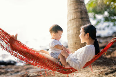 Mother with cute son sitting on hammock at beach