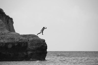 People on rock by sea against clear sky