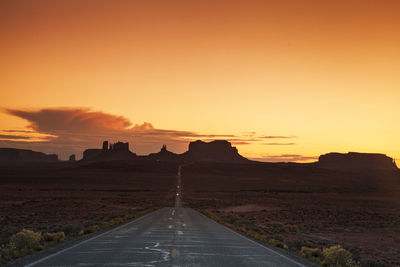 Empty road leading towards rock formations against orange sky