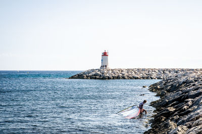 Lighthouse by sea against clear sky