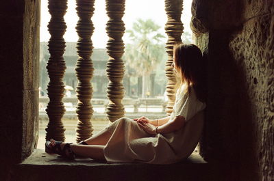 Side view of woman sitting on window