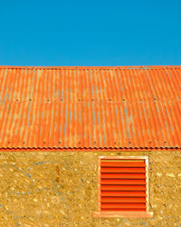 Close up of an old barn with corrugated iron roof and red shutters beneath clear blue sky