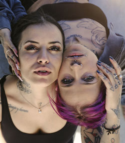 From above female friends with eccentric appearance and tattoos embracing on street and looking at camera