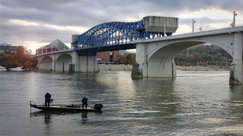People on bridge over river against sky