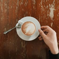 Cropped hand of person with coffee cup on wooden table