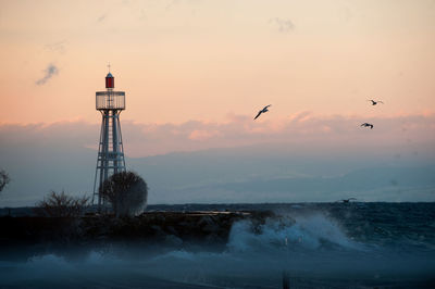 Lighthouse by sea against sky during sunset