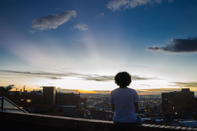 Rear view of silhouette woman against cityscape during sunset