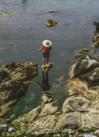 Rear view of woman standing on rock by lake