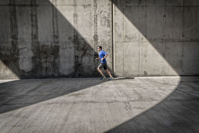 Side view full length of jogger on street against wall