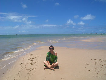 Portrait of happy woman sitting at beach against sky during sunny day