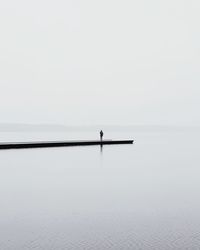 Silhouette person in swimming pool against sea against clear sky