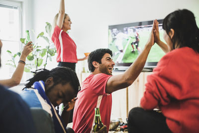 Young man sitting upset while red team celebrating victory at home